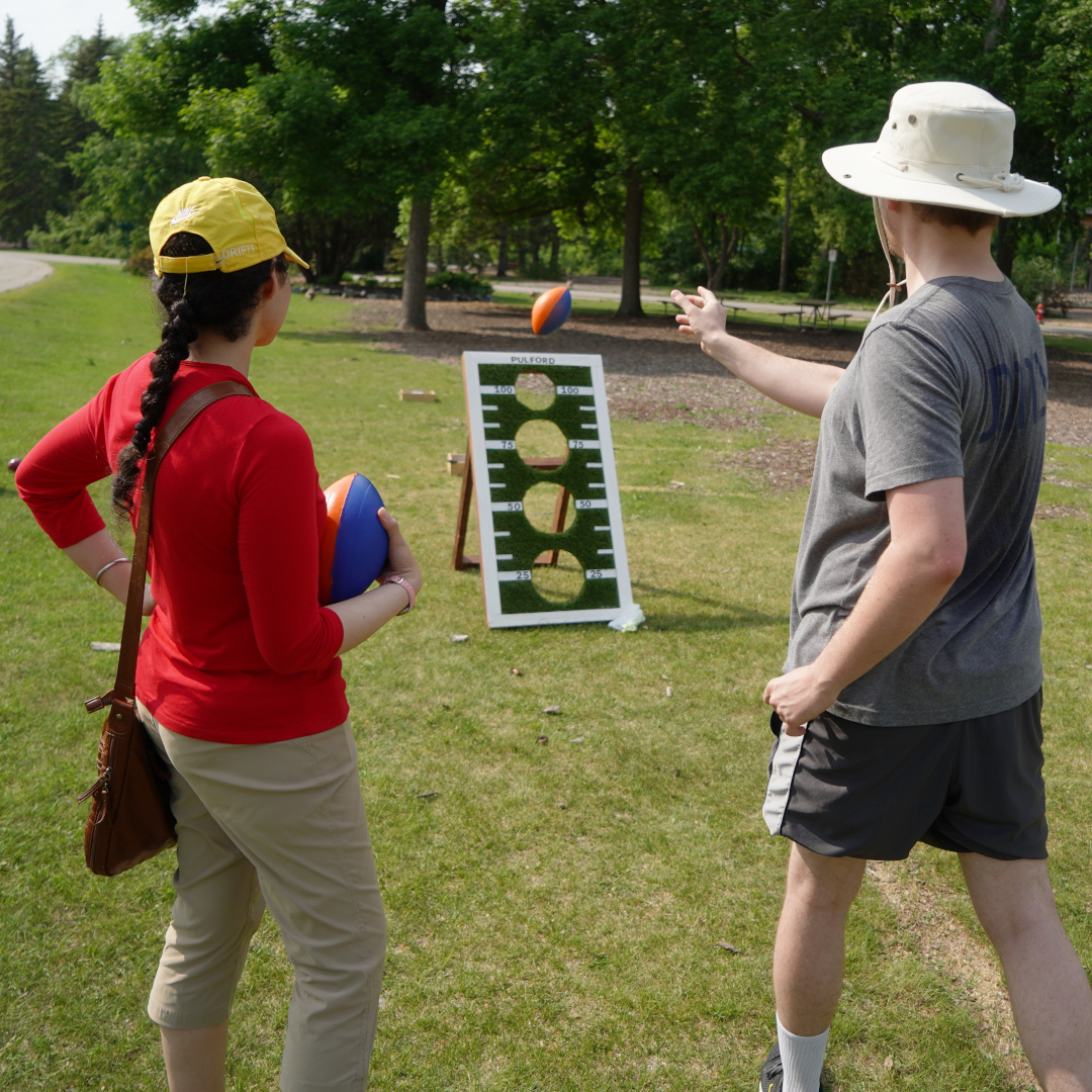 two people playing football toss, one is throwing a football at the green gameboard