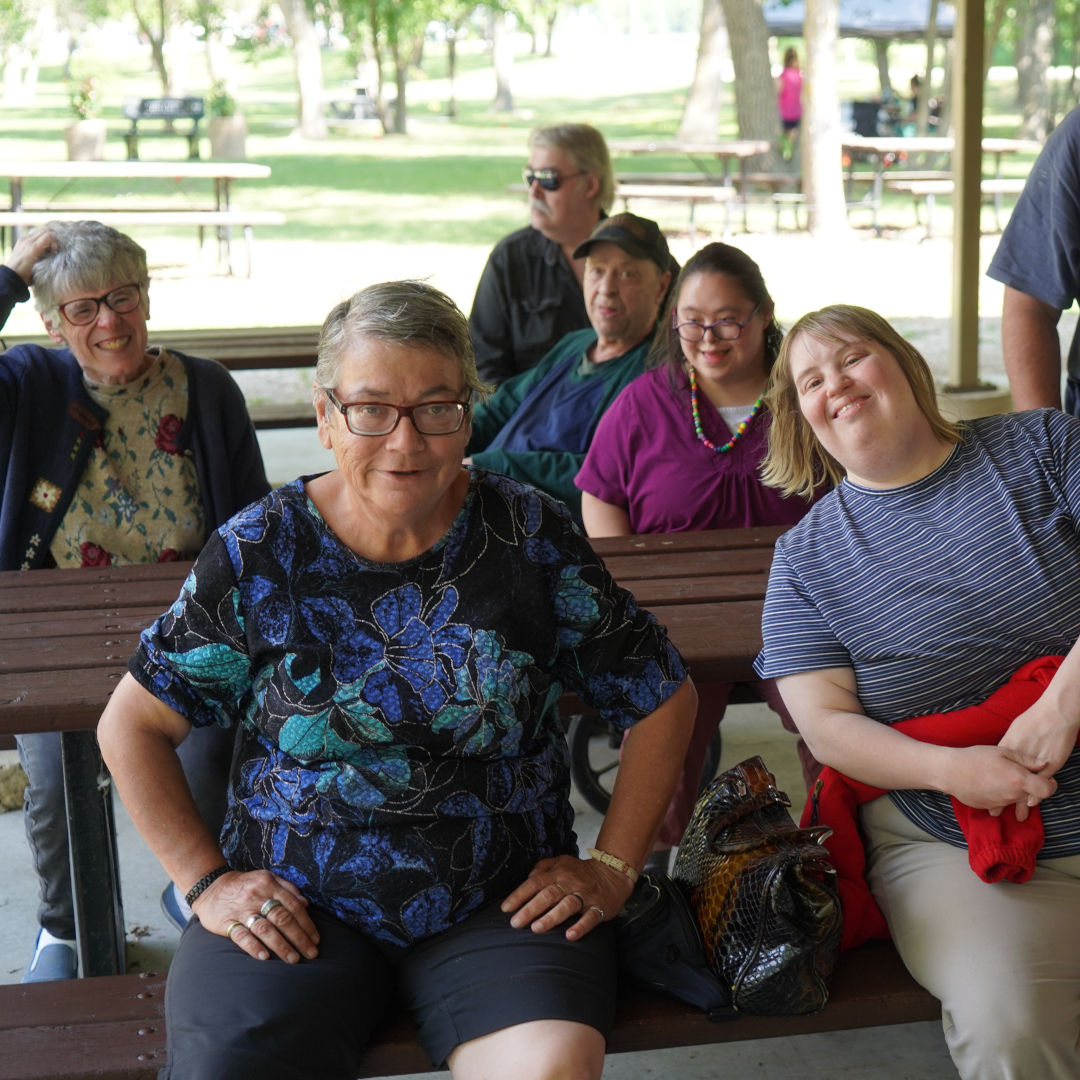 a group of smiling people sit around a picnic table